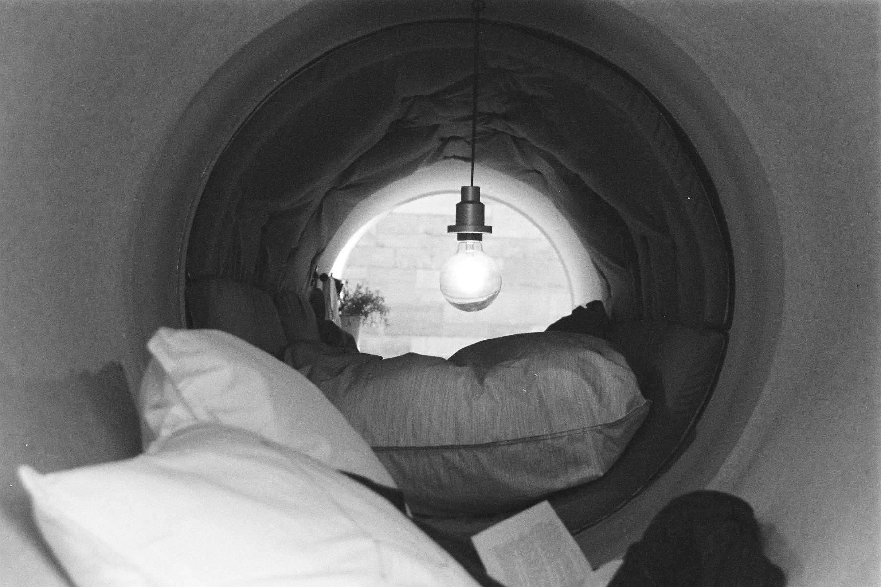 Kanalrohr, ausgestattet mit Polstern. Mittig hängt eine Glühbirne.